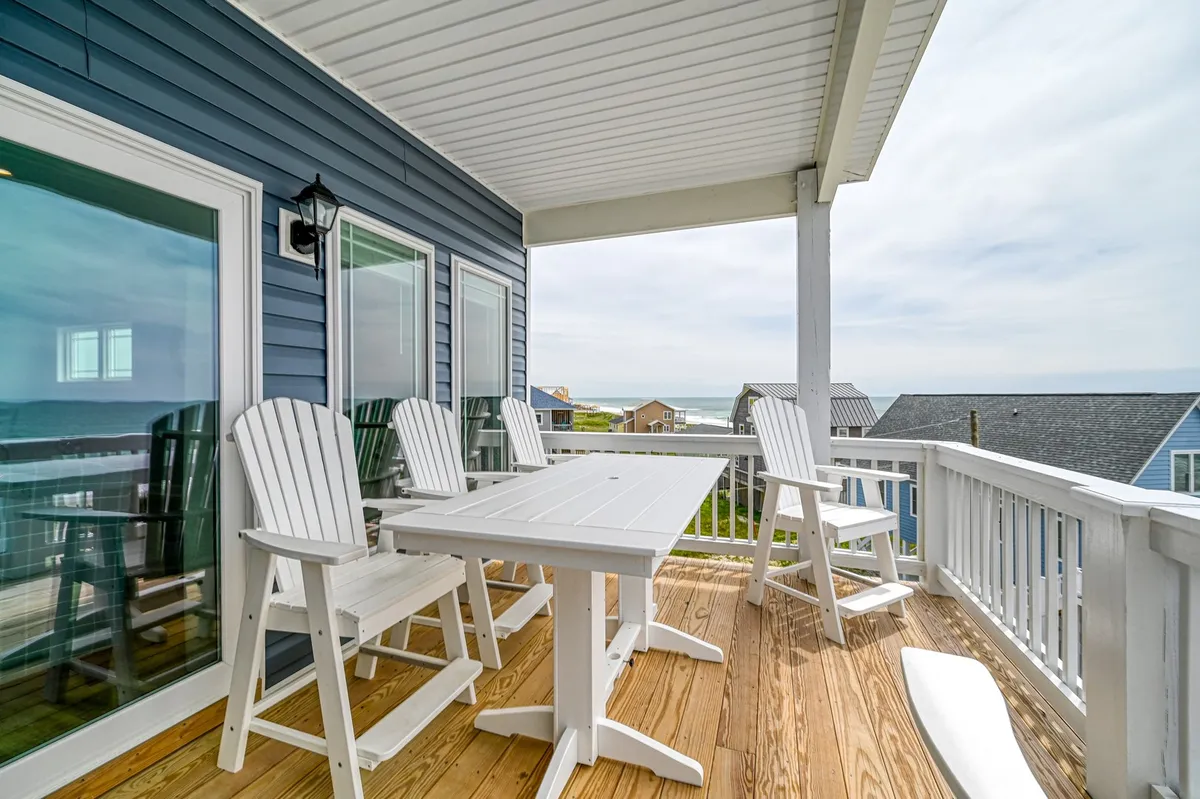 An outdoor dining table with Adirondack chairs set on a deck facing the vast ocean. The environment is ideal for al fresco dining, family gatherings, or simply enjoying the changing light as day turns to night.