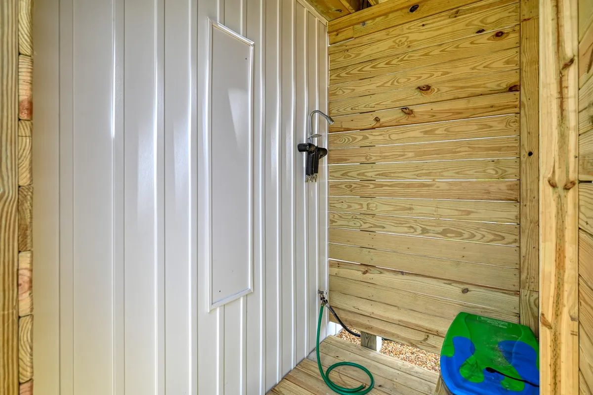 This image presents an outdoor shower with wooden walls and a simple green stool, emphasizing the ease of rinsing off after beach trips or outdoor activities.