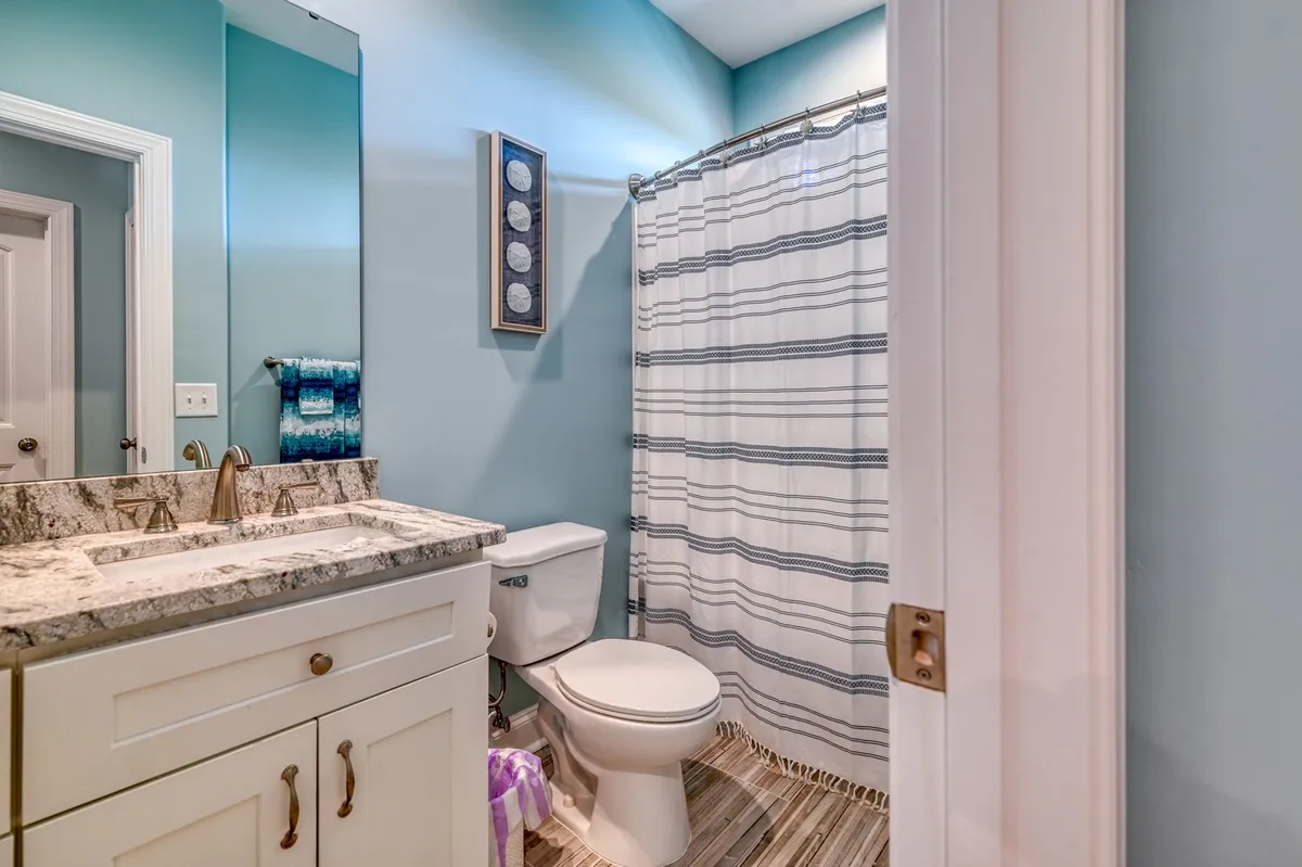 A refreshing and serene bathroom featuring a granite countertop, a striped shower curtain, and decorative wall art. The space is clean, bright, and ready for guests to use their own towels and toiletries.