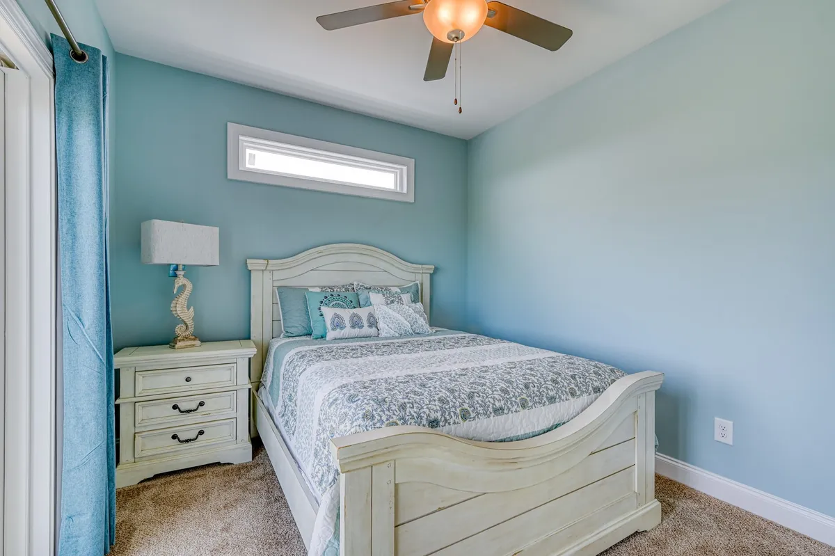 A calm and inviting bedroom with a bed dressed in decorative bedding, complemented by a bedside table with a lamp and elegant curtains. The room exudes tranquility and comfort, ideal for personalizing with your own linens.