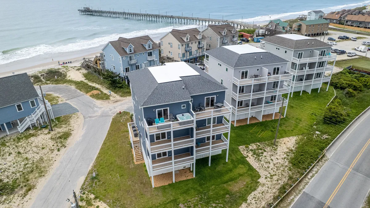 A sweeping exterior view of beachfront properties along North Topsail with the ocean waves rolling in and a pier stretching out into the water. The scene captures vibrant beach activity, the proximity of homes to the shore, and the inviting atmosphere of a classic beach day.