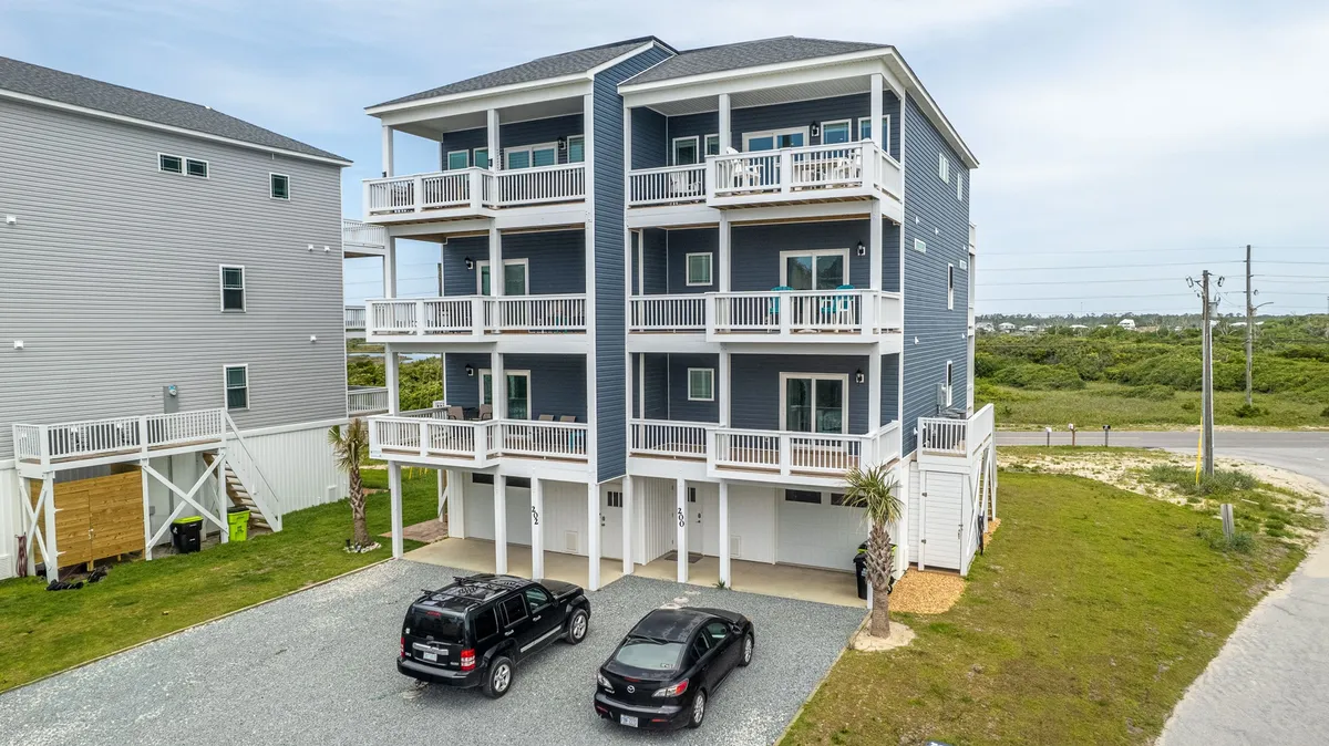 This image shows the building's exterior, highlighting the spacious driveway with parked vehicles, landscaped yard, and private balconies. The overall atmosphere is cheerful and welcoming, suggesting an easy arrival and offering a clear view of the entry experience.