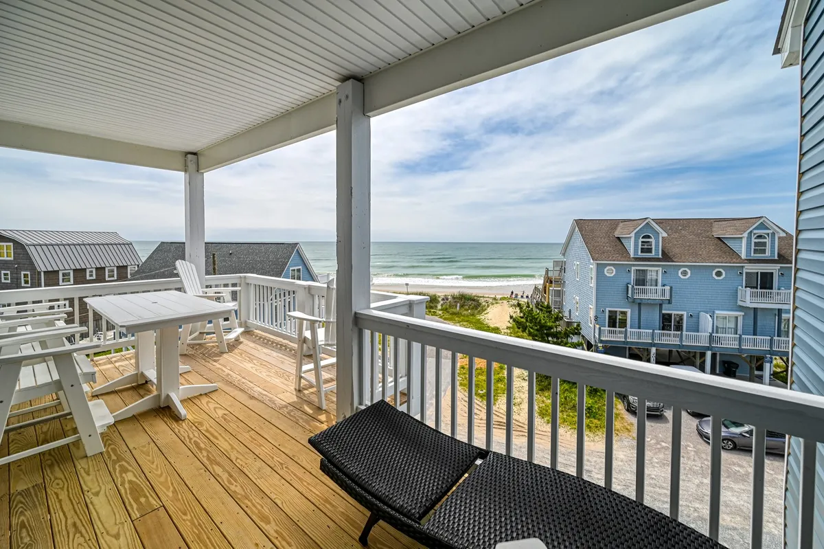 This image captures a sweeping view of the ocean from a deck furnished with comfortable outdoor seating, set up perfectly for sunbathing, outdoor dining, or simply watching the sunrise. The proximity to the beach and the expanse of sky and water highlight the seamless transition from indoor living to the coastal outdoors.