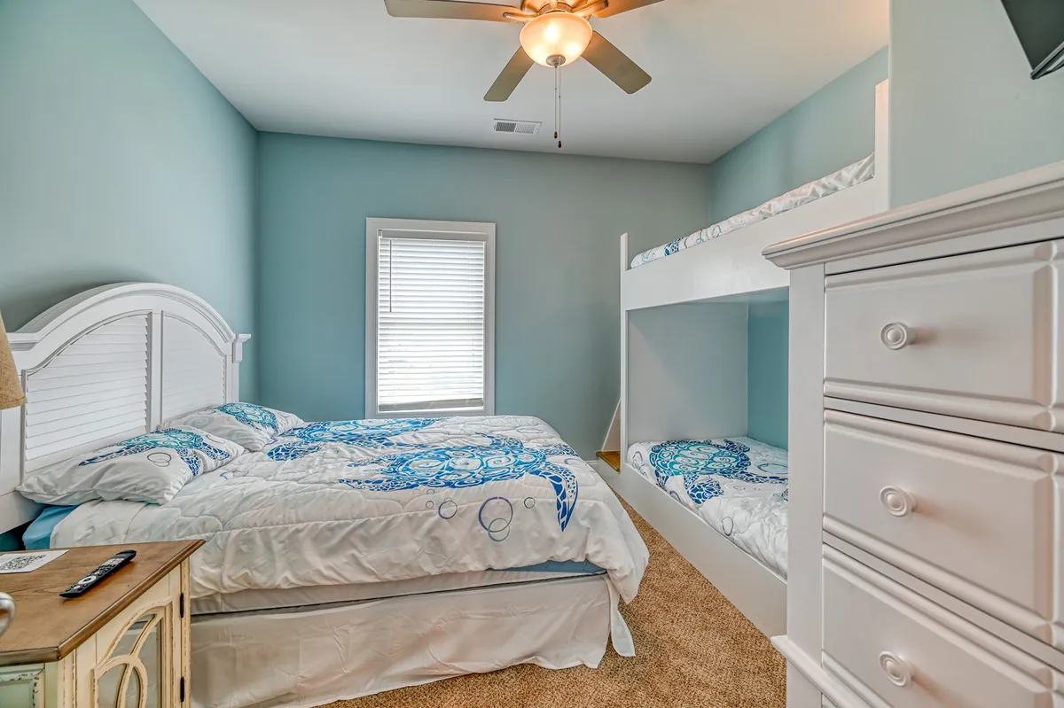 A cheerful and comfortable guest room featuring a queen bed and a bunk bed, a window letting in natural light, and a dresser. The room is set up for both adult and family use, making it perfect for families with children seeking flexibility and bonding opportunities.