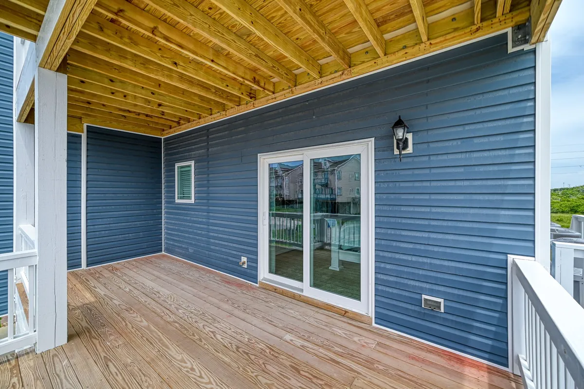 A relaxed exterior scene showcasing a wooden deck attached to a blue-sided home, featuring glass sliding doors opening to the outdoors. The deck is an inviting spot, ideal for enjoying morning coffee or reading a book while taking in the fresh air and views.