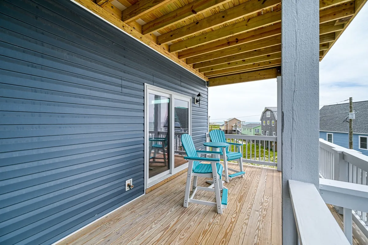 A tranquil wooden deck outfitted with blue chairs, overlooking what is likely a marsh or ocean view. The sliding glass doors suggest easy flow between indoor and outdoor spaces, inviting guests to relax, socialize, or simply take in the evening light and sunset views.